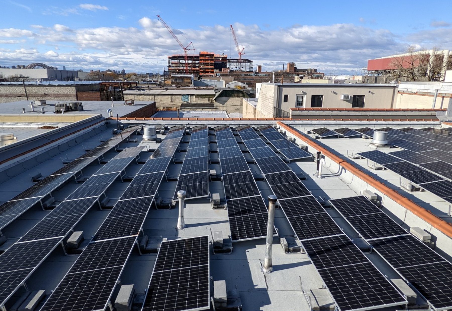 Rooftop solar array on a food production facility in Astoria, Queens, with the Hell Gate Bridge on the horizon
