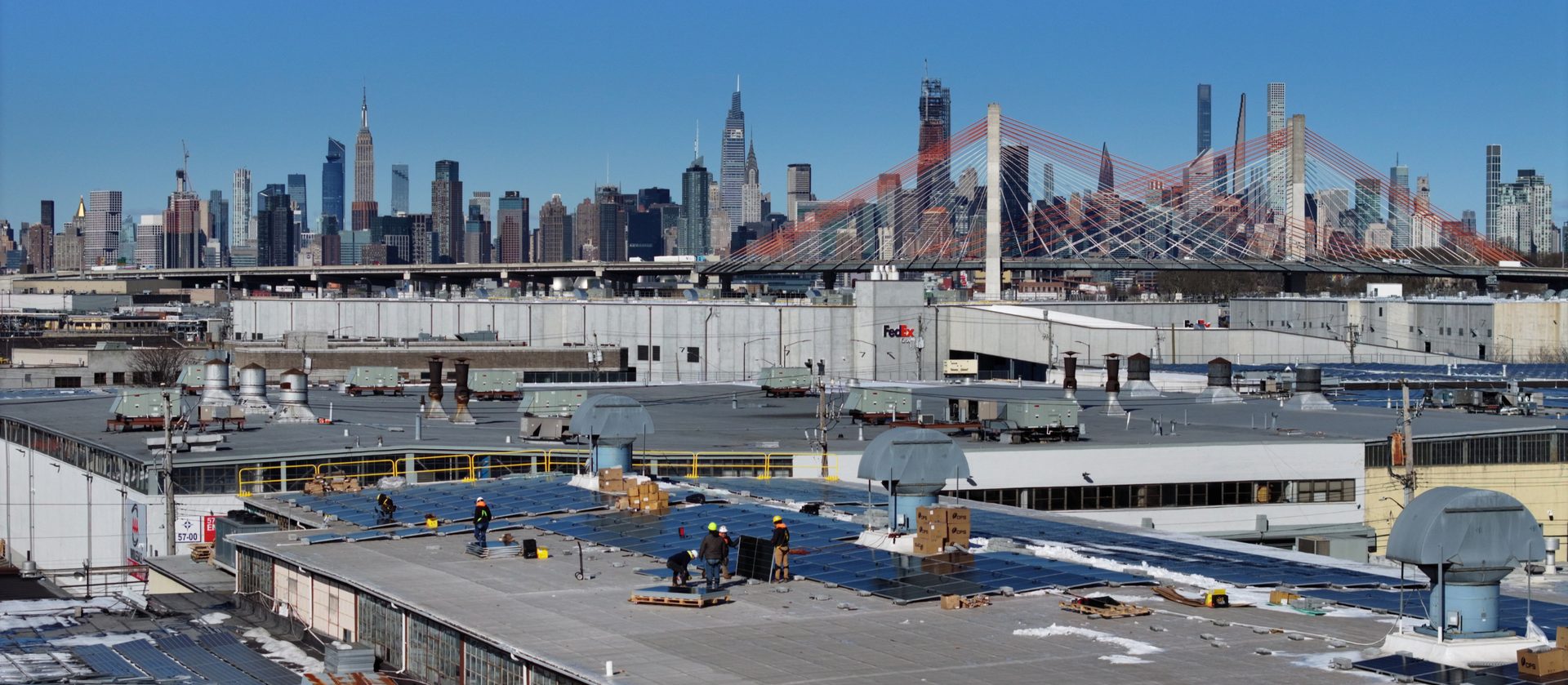 Bliss Solar crew installing panels on a Queens rooftop with the Kosciuszko Bridge and Manhattan skyline behind
